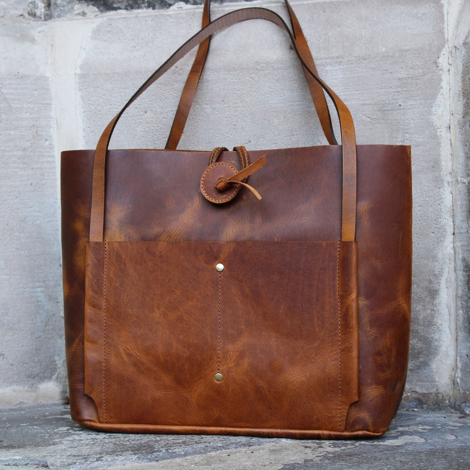 Introducing the Billy-Brown Leather Handbag, a sophisticated and exclusive tote bag crafted from luxurious buffalo leather in a unique distressed finish. With a quick access front and back sleeve, one main compartment, and an organizer panel for cards and phone, this unlined bag flawlessly blends style and functionality. Elevate your wardrobe with this elegant and tasteful bag.