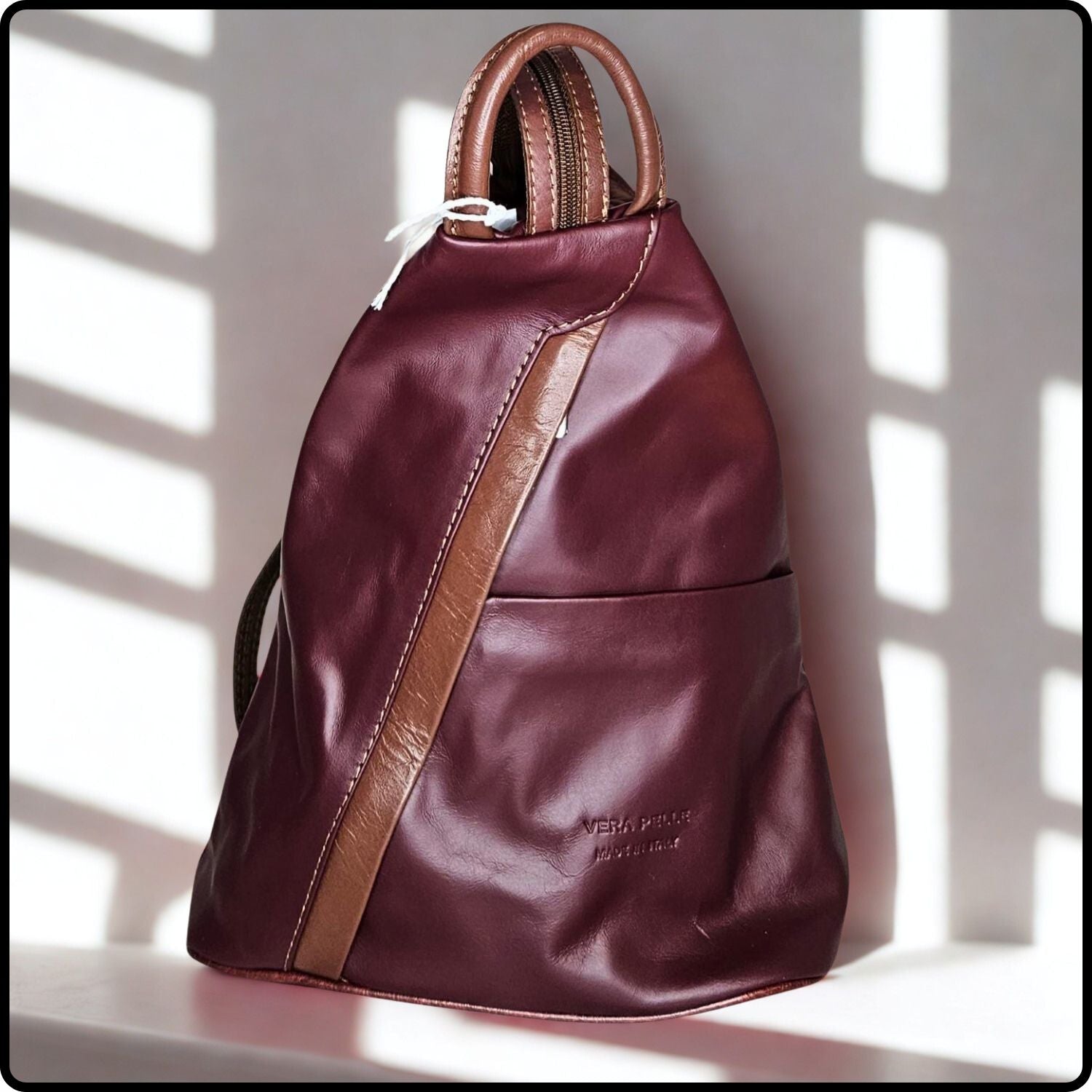 Maroon leather backpack with brown accents on a light background